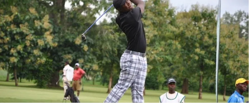 A Nigerian golfer swinging on a tree-lined fairway