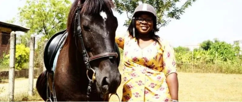 A Nigerian rider in a riding helmet standing with her horse at a riding club