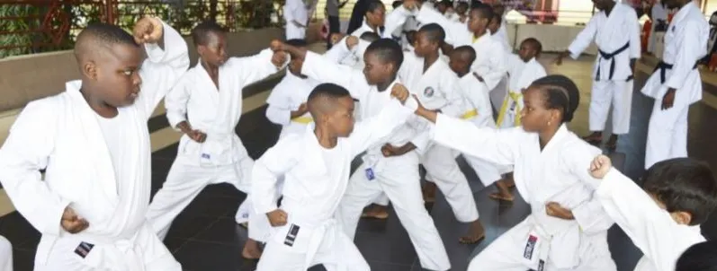 Children in white gis practising punches together in a Nigerian dojo