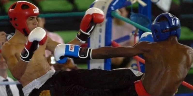 Two kickboxers in headguards exchanging kicks and punches