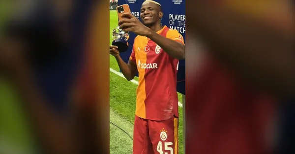 Victor Osimhen in a Galatasaray shirt holding a phone on the pitch