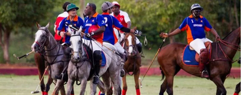 Polo players in blue, orange and white chase the ball on horseback at a Nigerian tournament